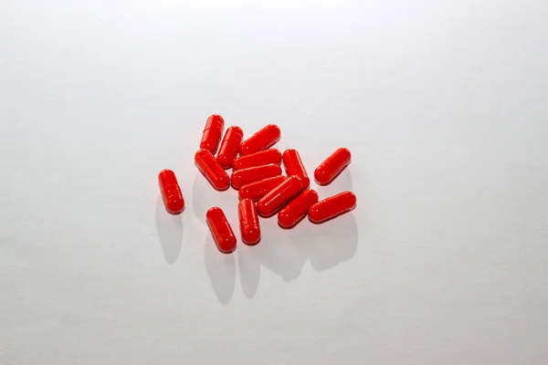 Розсіяні червоні таблетки на білому папері. Компонування спеціальних пропозицій, реклами, веб-фону. Концепція медицини, фармації, охорони здоров'я. Порожній простір для тексту, логотипу. Крупним планом, ізольовані ліки — стокове фото