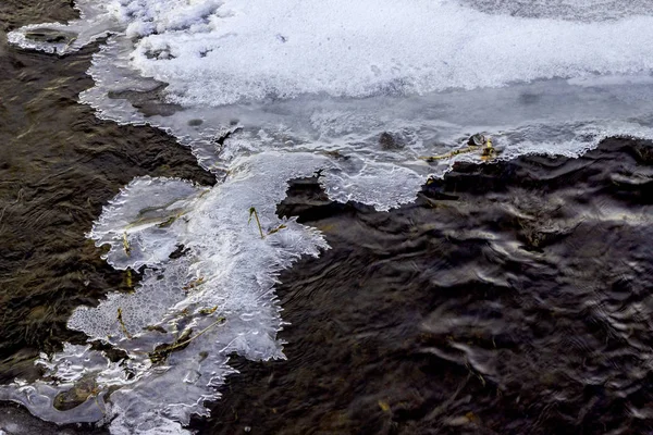 Glace sur la rivière en hiver. Gelée pittoresque, cristaux sur glace de rivière sur de l'eau sombre qui coule avec un fond transparent. La structure de la neige et la glace. Gros plan. Concentration sélective . — Photo