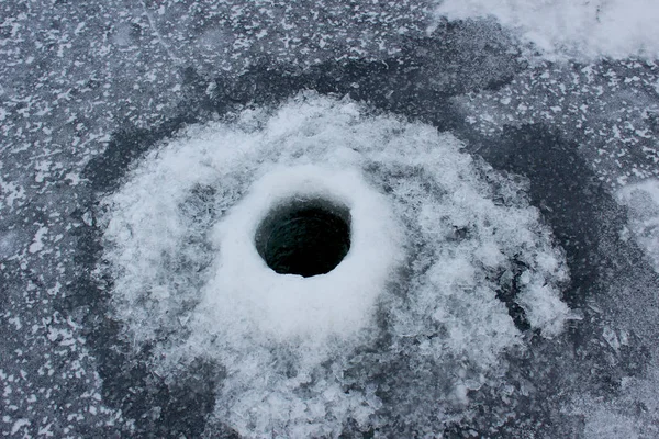 Wormwood, Ice hole in frozen water. A frozen hole drilled in ice with a drill. View from above. A frozen hole in a river. Winter fishing