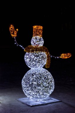 Kış gecesi şehrinde parlak bir çelenkten gelen kardan adam. Davetiyeler, selamlar, fotokopi alanı için harika bir arka plan. Kardan Adam Günü, 18 Ocak, Yeni Yıl ve sokakta Noel dekoru. Dikey fotoğraf