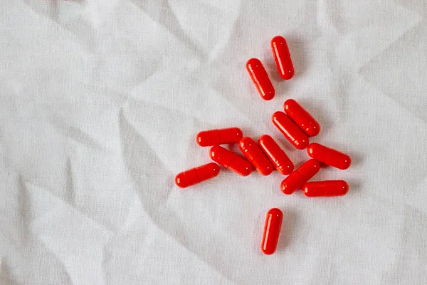 Red pills on a white cloth. Photo background with capsules on a fabric texture. Copy space, place for text — 图库照片