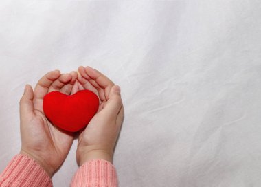 Hafif bir bezin üzerinde kırmızı kalpli bir çocuğun elleri. Kız elleri, beyaz arka planda izole edilmiş kırmızı bir kalp tutar. Anneler Günü için konsept, sağlık ve bakım. Sevgililer günü, bebeğim.