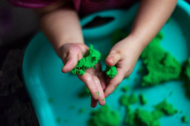 Yeşil sihirli kumla oynayan bir çocuğun elleri. Çocuk ödevi. Küçük kız kinetik kumla oynuyor. Yeşil kum havuzundaki kinetik kum. Yumuşak odak