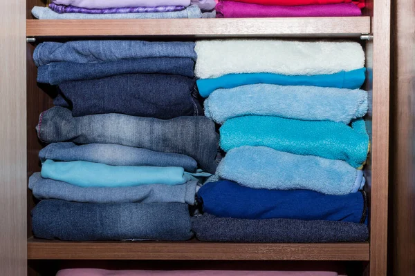 Shelving with warm boy clothes. A wooden cupboard with a stack of blue dark things. Shelf cabinet with folded things. Maintain order in the closet
