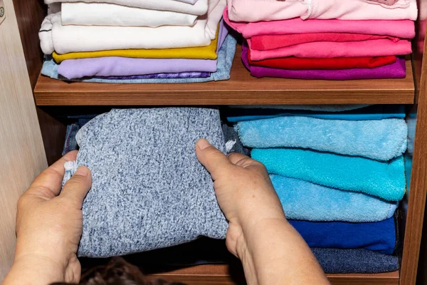 Women\'s hands put clean clothes on a shelf in a closet at home. A woman puts baby clothes on a bookcase. House cleaning, order, accuracy in the wardrobe.