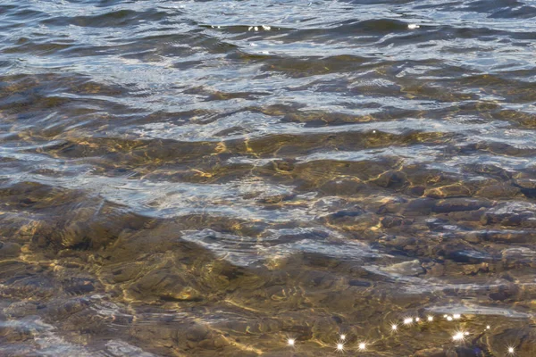 Beautiful clean river with a translucent stone bottom. The texture of the transparent water of a sea lake with small waves. Ripples of water from the wind. Fresh water of a forest lake on a sunny day.