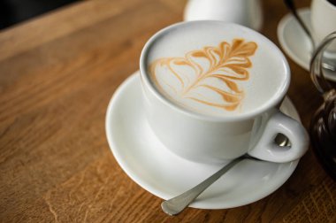 Kafedeki ahşap bir masanın üzerinde bir fincan kapuçino..