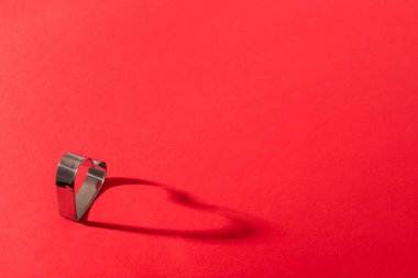 Kırmızı arkaplanda kalp şeklinde metal bir şekil ve uzayı kopyala. Sevgililer Günü konsepti. Gölgeli bir fotoğraf.