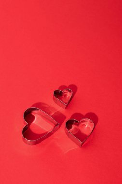 Sağ üst köşede kırmızı arka planı ve sevgililer günü için kopyalama alanı olan üç kalp şeklinde metal şekiller var.