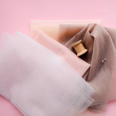 Düz yatıyordu. Arka planda kalın pembe çiçekler, iğneler ve iplikler var. Pastel renkler.