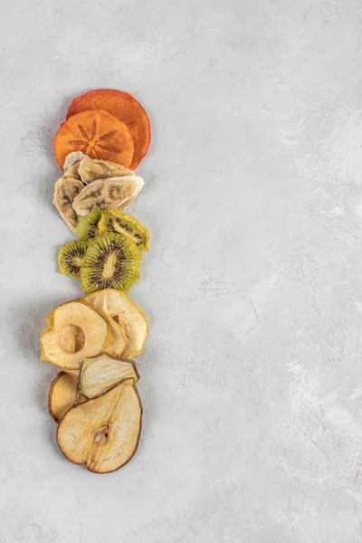 Healthy homemade fruit chips from apple, persimmon, pear, kiwi and banana on grey background. Organic diet food. The vegan diet. Dried fruits. Vegetarian plant based snack concept. Vertical frame