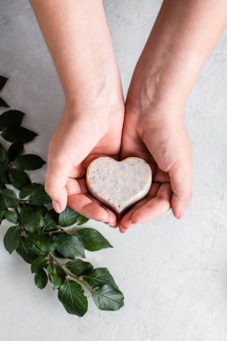 Gri arka planda bir kızın ellerinde kalp şeklinde sabun bulunan düz kompozisyon. Kişisel temizlik..
