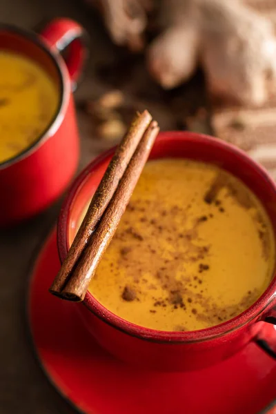 Cinnamon stick on a red cup of golden milk with turmeric powder against dark background. Close-up. A healthy drink to enhance immunity. Healthy drink. Super food — Stock Photo, Image