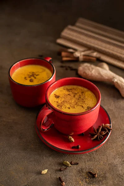 Red cup of golden milk with turmeric powder and cinnamon on a dark background. A healthy drink to enhance immunity. Healthy drink. Super food — Stock Photo, Image