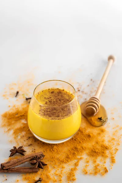 Beautiful glass with golden milk, honey, cinnamon and other ingredients on a white background. Healthy drink. Strengthening immunity. Antioxidant and superfood. — Stock Photo, Image