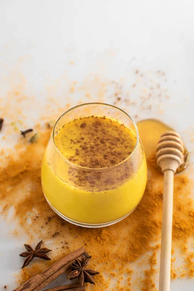 A glass of golden milk with honey, cinnamon and other ingredients on a white background. Healthy drink. Strengthening immunity. Antioxidant and superfood. — Stock Photo, Image