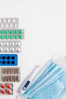 Kabarcık paketlerinde renkli haplar ve kapsüller, beyaz arka planda termometre ve koruyucu maske. Coronavirus. İlaç endüstrisi..