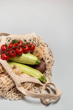 Gri arka planda tekrar kullanılabilir bir çantada çevre dostu sebzeler. Çevresindekilerle ilgilenmek ve plastiğin reddedilmesi. Boşluğu kopyala