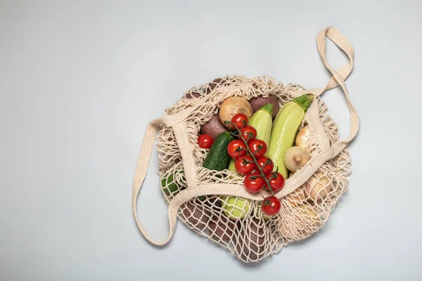 Gri arka planda tekrar kullanılabilir bir çantada çevre dostu sebzeler. Çevresindekilerle ilgilenmek ve plastiğin reddedilmesi. Boşluğu kopyala