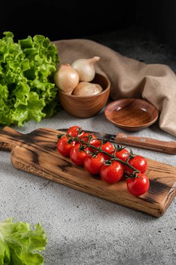 Tahtadaki kiraz domatesleri, diğer sebzelerle birlikte gri arka plan. Çiftlik ürünleri.