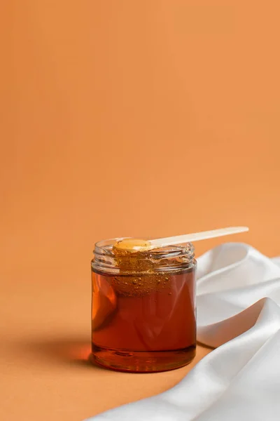 Un recipiente con pasta de azúcar para eliminar el cabello sobre un fondo cálido, una espátula de madera con cera. Spa y Shugaring. El concepto de belleza y autocuidado —  Fotos de Stock