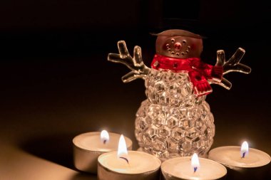 Kırmızı eşarplı, siyah şapkalı ve gülen yüzlü şirin bir yılbaşı kardan adam Noel arifesinde sıcak mum ışığıyla çevrili gelecek zamanı ve Noel zamanını kutlamaya hazır.