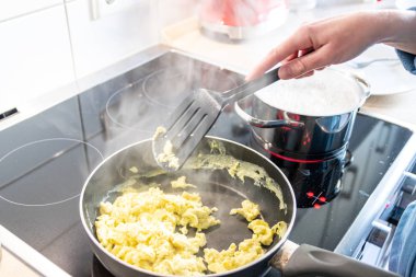 Woman and mother cooking a delicious omelette for her family in the kitchen with a hot pan on the ceran stove as healthy protein food based on fresh eggs as yummy brunch or lunch clipart