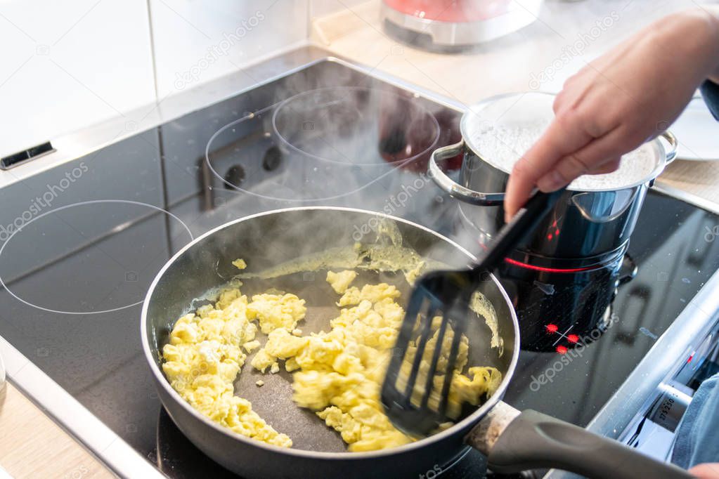 Woman and mother cooking a delicious omelette for her family in the kitchen with a hot pan on the ceran stove as healthy protein food based on fresh eggs as yummy brunch or lunch