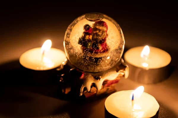 Santa Claus in a stormy snowstorm globe on his way to christmas with a lot of presents for the children and surrounded by burning tea light candles as atmospheric advent time decoration