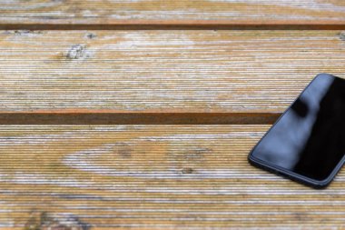 Disturbance in reception with black smartphone and touch device with a clean reflecting surface in need of a ruggedized case for the cellular and mobile device lying on the wooden table