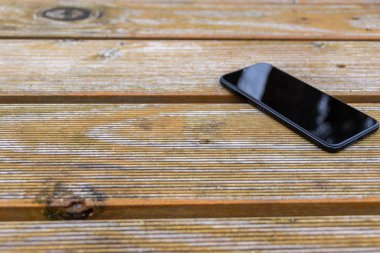 Disturbance in reception with black smartphone and touch device with a clean reflecting surface in need of a ruggedized case for the cellular and mobile device lying on the wooden table