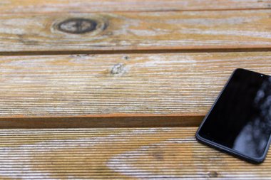Disturbance in reception with black smartphone and touch device with a clean reflecting surface in need of a ruggedized case for the cellular and mobile device lying on the wooden table