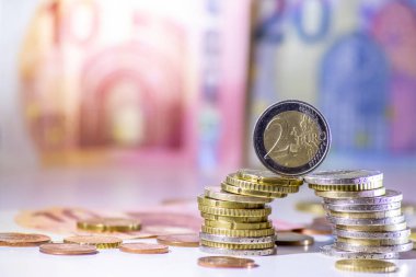 Arka plandaki Avrupa sikkeleri yığını ve banka notları, Avro ve Avrupa, Avrupa ticaret ve mali ticaretinin yanı sıra tasarruf, mali başarı ve kredi yönetimi ile uluslararası finansmanı gösteriyor
