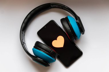 Siyah ekranda kırmızı kalpli siyah akıllı telefon ve kulaklık üzerinde kablosuz mavi telefon mobil müzik akışı, sağlık kontrolü, akıllı telefon bağımlılığı, müzik sevgisi ve müzik dinlemeyi gösteriyor.