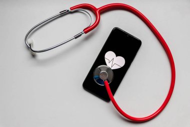 Kalp sembolü ve kalp atışı olan stetoskop ve siyah akıllı telefon dijital doktorların ofisini, dijital teşhisi ve sağlık takip cihazını, sağlık istatistiklerini ve sağlık asistanlarının ilaçlarını gösteriyor.