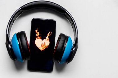 Siyah bir akıllı telefon ekranında yanan alevlerle yanan kalp sembolü ve kulaklık ve fotokopi alanı müzik ve mobil müzik ve müzik dinleme hizmetlerini gösteriyor.