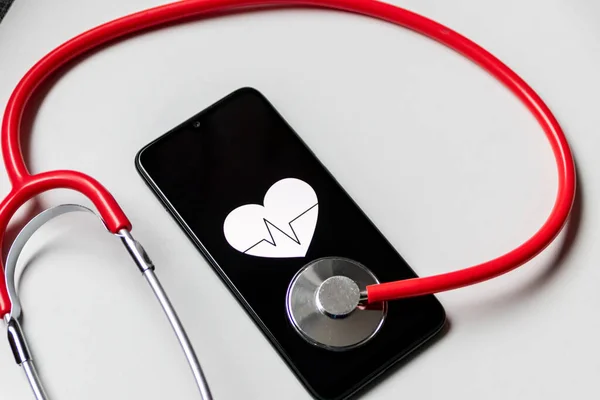 Stethoscope and black smartphone with a heart symbol and heartbeat to show digital doctors office, digital diagnosis and health tracker as well as health statistics and health assistants medication