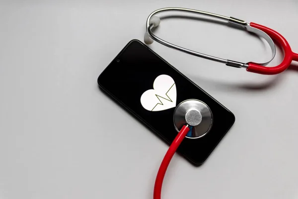 Stethoscope and black smartphone with a heart symbol and heartbeat to show digital doctors office, digital diagnosis and health tracker as well as health statistics and health assistants medication