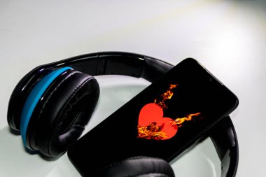 Siyah bir akıllı telefon ekranında yanan alevlerle yanan kalp sembolü ve kulaklık ve fotokopi alanı müzik ve mobil müzik ve müzik dinleme hizmetlerini gösteriyor.