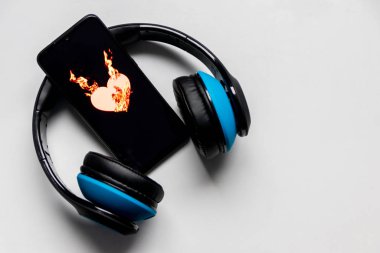Siyah bir akıllı telefon ekranında yanan alevlerle yanan kalp sembolü ve kulaklık ve fotokopi alanı müzik ve mobil müzik ve müzik dinleme hizmetlerini gösteriyor.