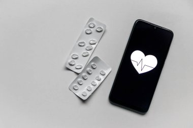 Beyaz arka planda hapları olan akıllı telefon ve tıbbi sağlık ve sağlık izleme uygulamaları veya dijital sağlık uygulamaları ve dijital sağlık uygulamaları ve dijital ilaçlar için kalp atışı olan kalp şekli sergilenmekte.