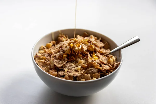 Healthy breakfast with golden honey floating over cornflakes with walnuts as delicious and dieting oatmeal with a silver spoon for organic and vegetarians serving in the morning natural ingredients