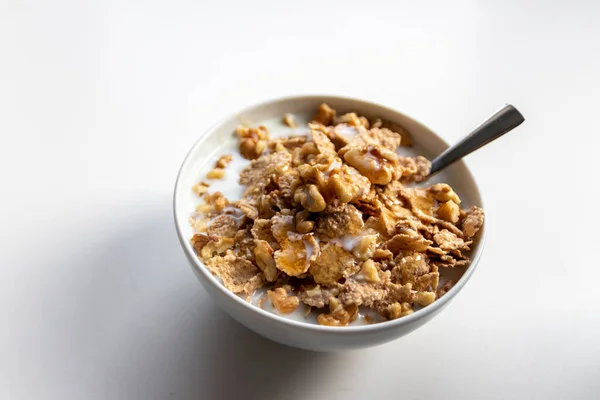 Healthy breakfast in a white bowl with golden honey floating over cornflakes with walnuts and milk as delicious oatmeal with a silver spoon for organic and vegetarians serving natural ingredients