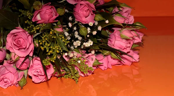 Green bouquet with small roses on an orange background. Pink small roses.