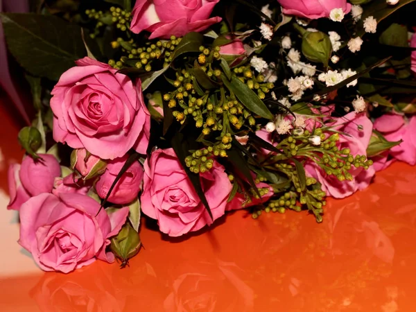 Green bouquet with small roses on an orange background. Pink small roses.