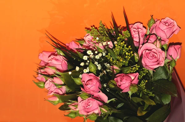 Green bouquet with small roses on an orange background. Pink small roses.