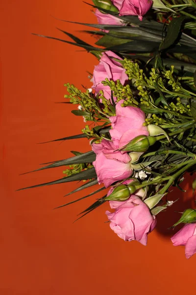 Green bouquet with small roses on an orange background. Pink small roses.