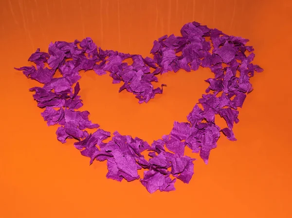 Purple heart on an orange background. A heart made of pieces of paper.
