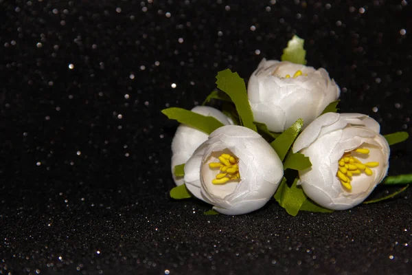 A bouquet of white artificial flowers on a black shiny background.