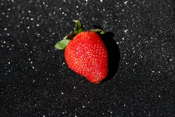 One strawberry on a black background. Berry on a black shiny background.